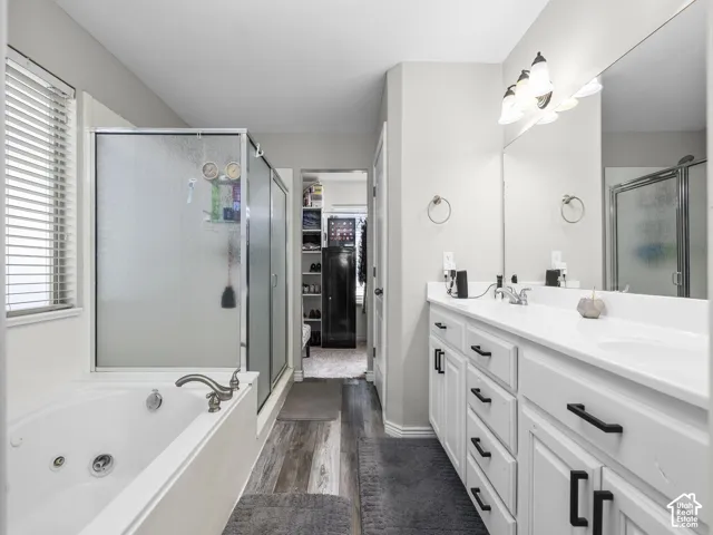 Dual vanity with white countertop and integrated sinks, white cabinetry with black hardware, jetted soaking tub, and a separate shower with frosted glass enclosure