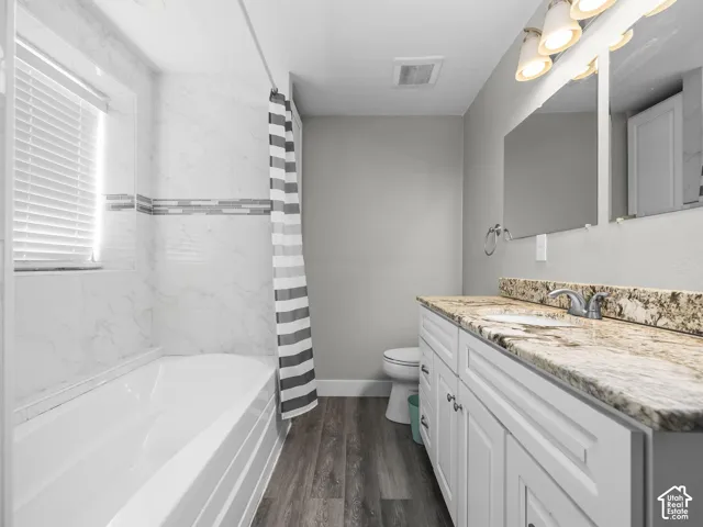 Spacious bathroom featuring a double vanity with stone countertop, white cabinetry, wood-finish flooring, and a tiled shower/tub combination