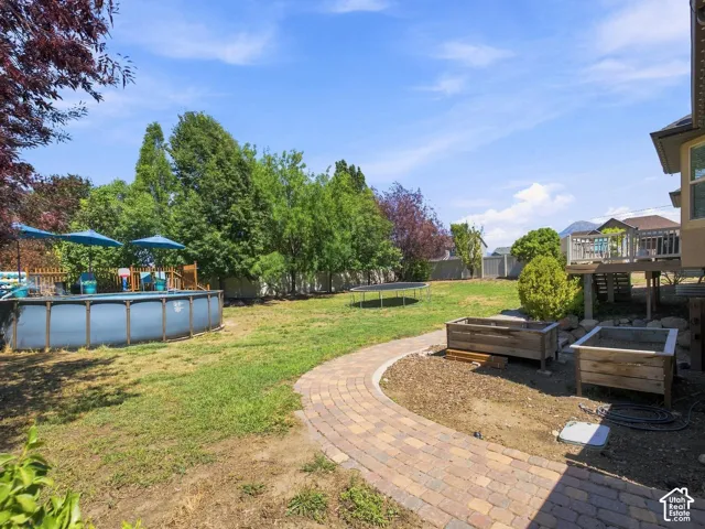 Expansive yard featuring a paver pathway, elevated wooden deck, above-ground pool, and a trampoline