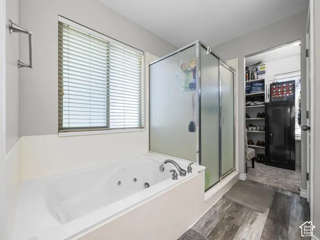 Soaking tub with a built-in faucet, frosted glass shower enclosure, wood-finish flooring, and a window with blinds