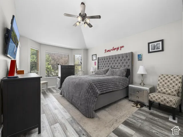 Vaulted ceiling with a ceiling fan, wood-finish flooring, and multiple windows