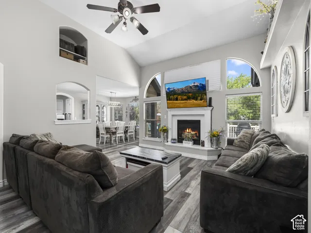 Vaulted ceiling with a ceiling fan, fireplace with a mantel, wood-finish flooring, and multiple windows