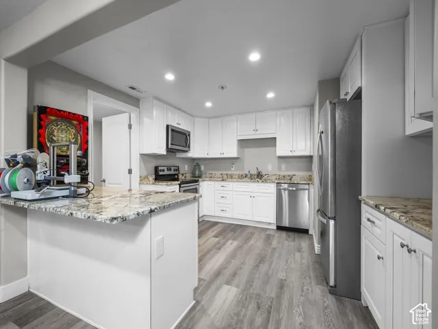 White cabinetry, stainless steel appliances, recessed lighting, wood-finish flooring, and stone countertops