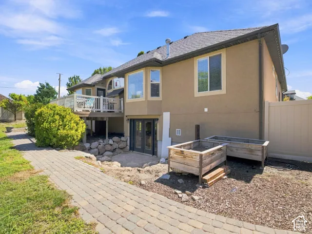 Stucco exterior featuring a second-story deck with white railing, paved walkway, two raised garden beds, and double glass-panel doors