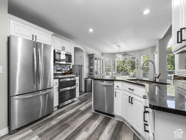 White cabinetry with modern black hardware, stainless steel appliances, dark countertops, wood-finish flooring, and recessed lighting