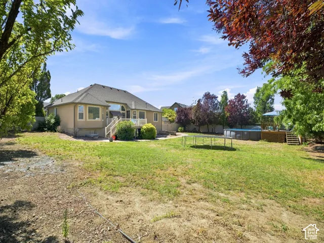 Expansive backyard featuring a manicured lawn, a raised wooden deck with stairs, a built-in above-ground pool, and mature perimeter trees