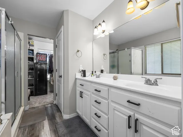 Dual vanity with white cabinetry and matte black hardware, wood-finish flooring, and a mirrored wall