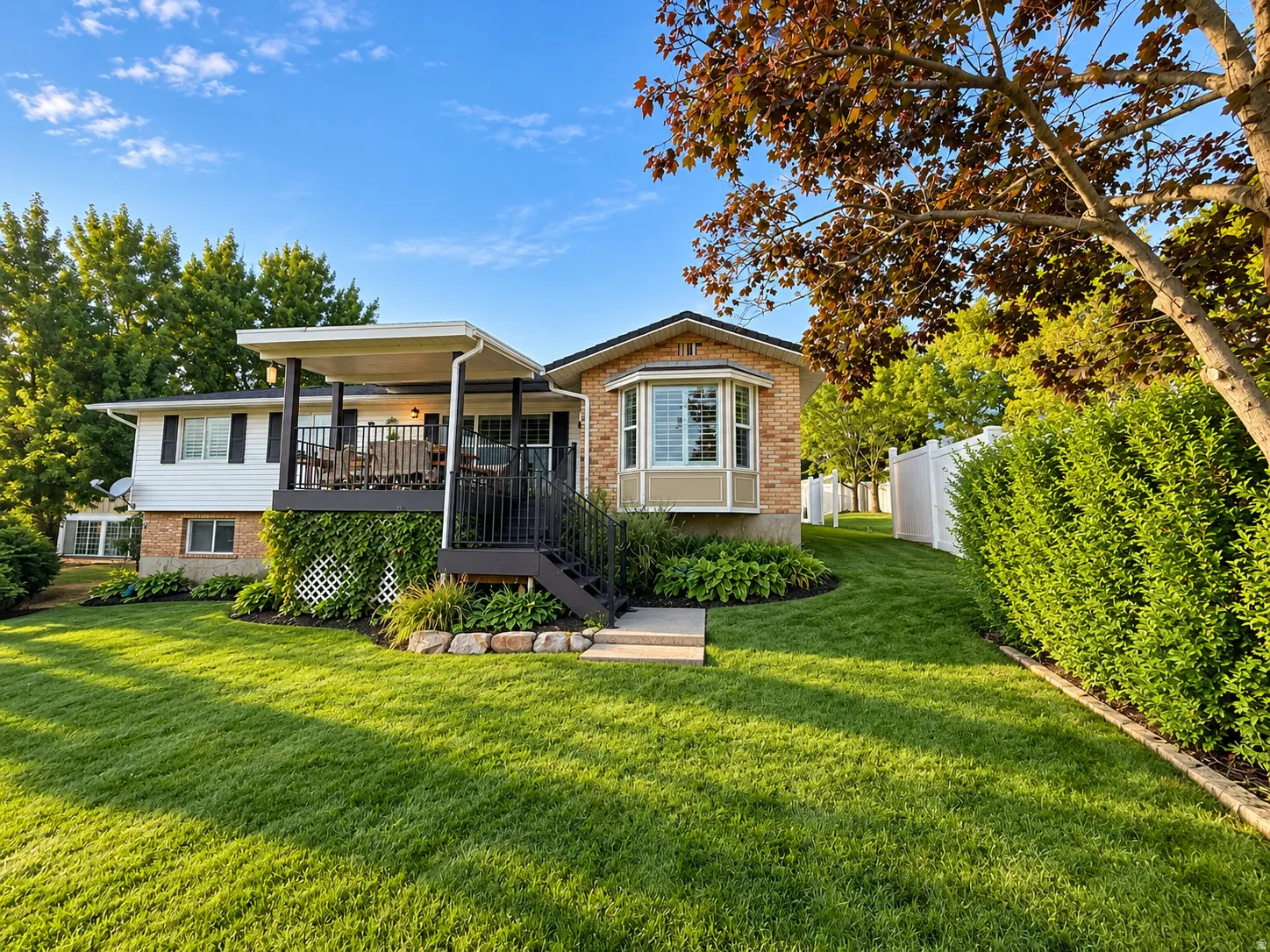 Expansive lawn with mature landscaping, covered deck, and brick bay window