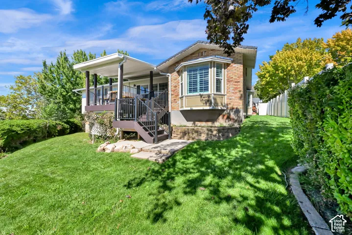 Brick exterior with a bay window, covered elevated deck, dark railings, and a manicured lawn