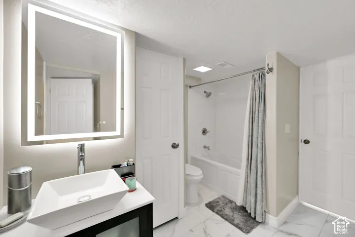 Backlit vanity mirror, vessel sink, polished chrome faucet, white tile flooring, and integrated bathtub with shower