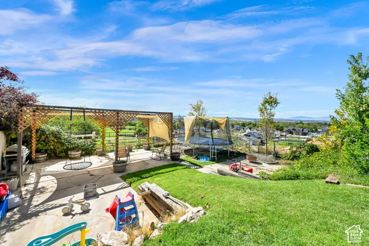 Expansive outdoor patio with a wooden lattice pergola, concrete surface, and tiered grassy areas