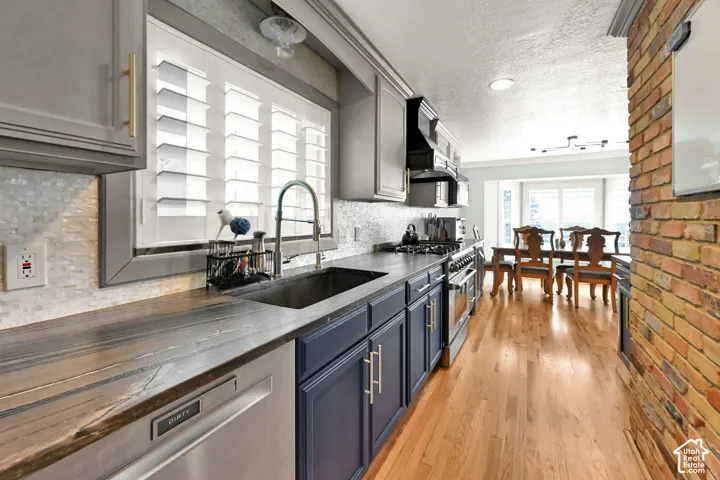 Kitchen featuring wood-finish countertops, stainless steel appliances, a tile backsplash, and a large window with plantation shutters