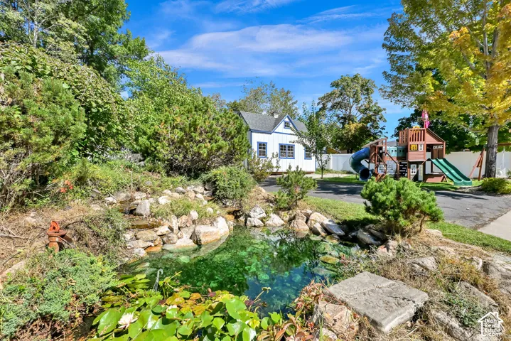 Landscaped backyard featuring a tranquil pond with water lilies, stone edging, and mature plantings