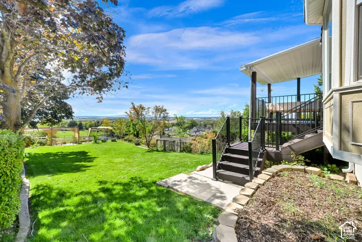 Expansive lawn with mature landscaping, a covered outdoor deck, and a multi-level wooden staircase with black railings