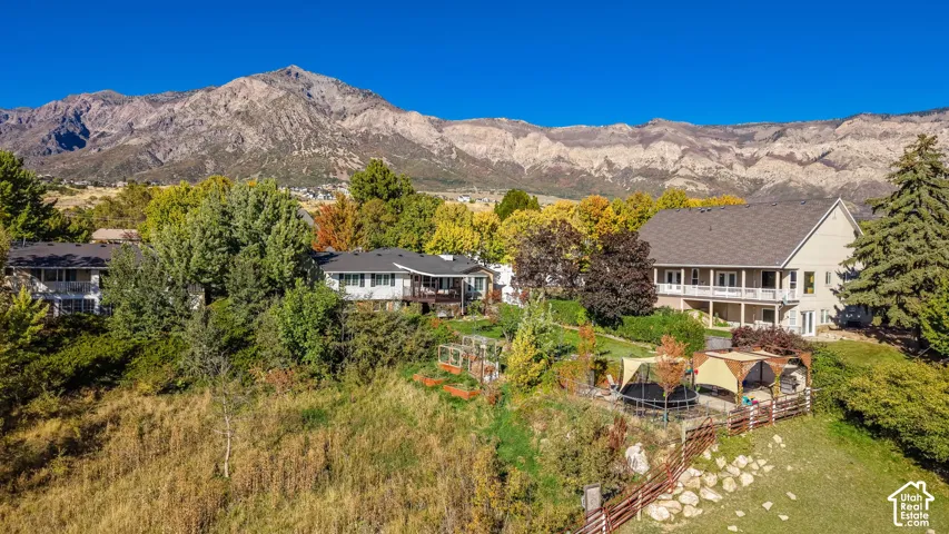 Expansive property featuring a multi-level structure with a covered balcony, a separate structure with a deck, mature trees, and mountainous terrain in the background