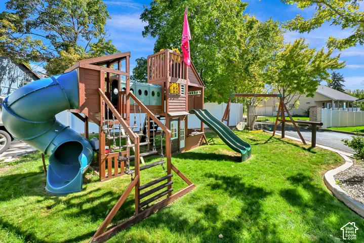 Expansive green lawn with a multi-level playset featuring a tunnel slide and swings