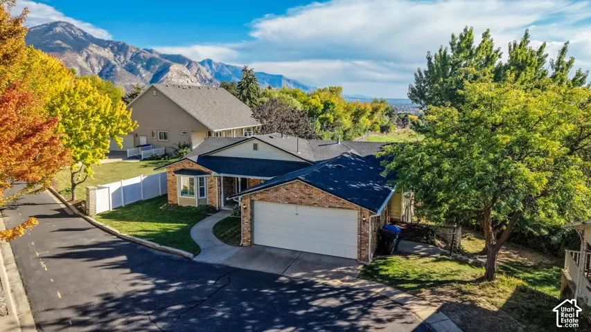 Brick exterior with an attached two-car garage, concrete driveway, and established landscaping