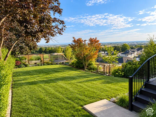 Expansive backyard featuring a manicured lawn, established perimeter landscaping, decorative wood fencing, and a multi-level deck with black railings