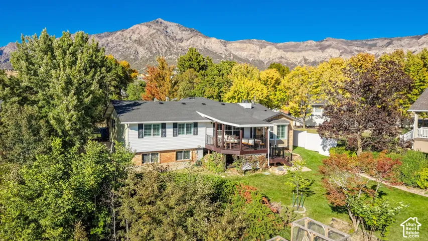 Mountain backdrop, elevated deck, manicured lawn, established landscaping, and dark shingle roof