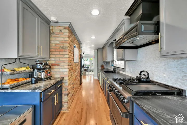 Wood-finish flooring, exposed brick wall, sleek cabinetry, stone countertops, and stainless steel range