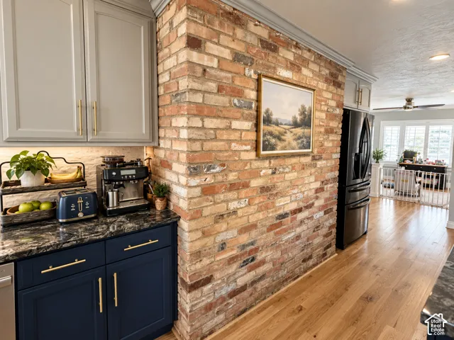 Exposed brick accent wall, wood-finish flooring, two-tone cabinetry with gold-tone hardware, dark countertop, and recessed lighting