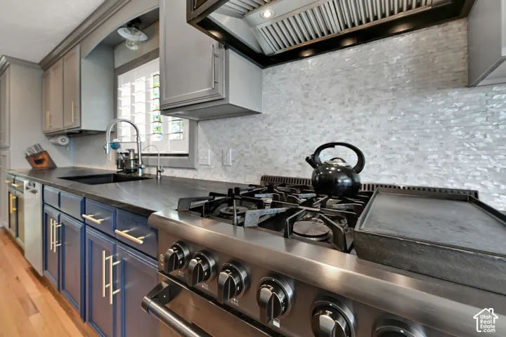 Stainless steel professional-grade range, iridescent tile backsplash, under-cabinet lighting, and custom two-tone cabinetry with gold-finish hardware