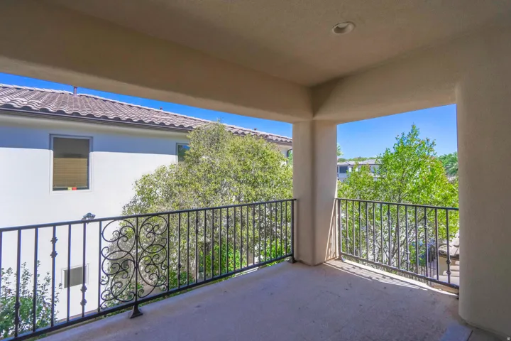 Covered balcony with decorative wrought iron railing, recessed lighting, and stucco exterior walls