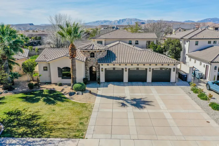 Stucco exterior with stone accents, a tile roof, a three-car garage, and a paver driveway