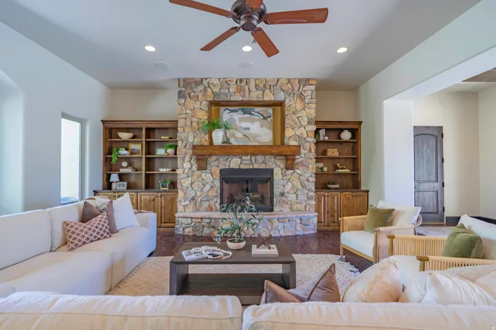 Stone fireplace with wood mantel, built-in shelving, recessed lighting, and wood-finish flooring
