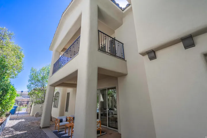 Stucco exterior featuring an upper balcony with iron railings, a covered patio, and sliding glass doors