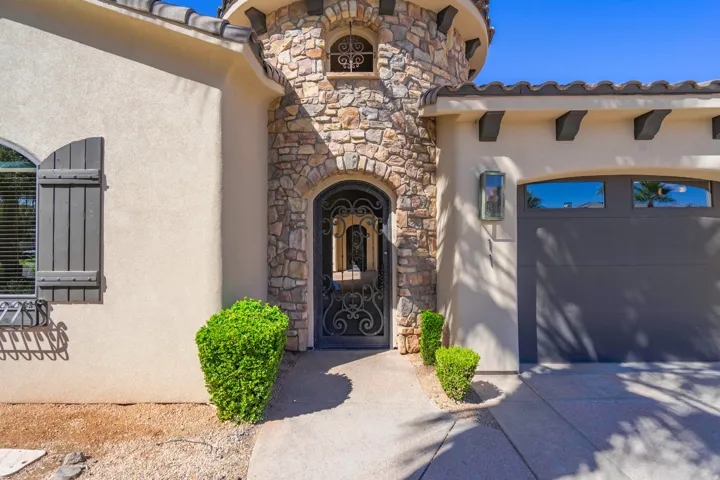 Stone veneer facade with arched entry, wrought iron door, decorative window shutters, and a garage with transom windows
