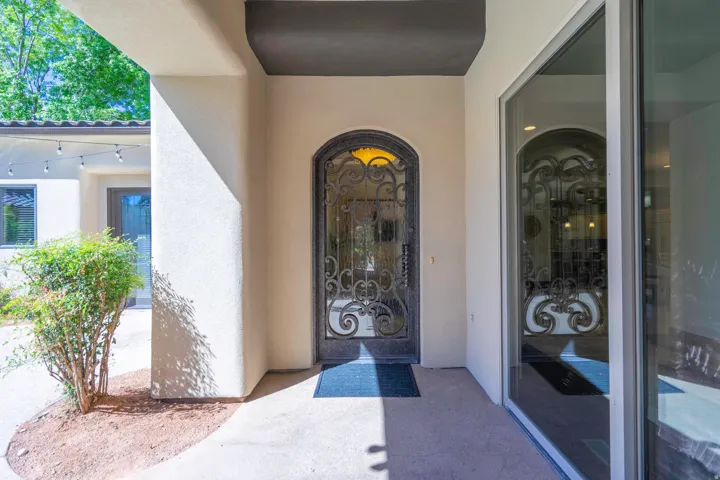 Arched iron and glass entry door, stucco exterior, concrete walkway, and established landscaping