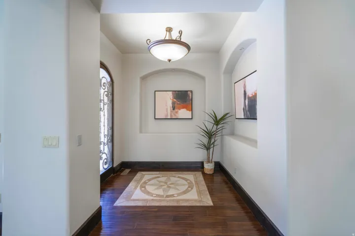 Entrance featuring a decorative iron door, wood-finish flooring, recessed wall niches, and a central medallion tile inlay