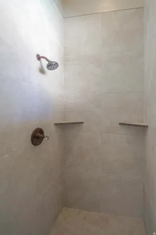Tiled shower enclosure featuring a bronze-finish shower head and control, and two built-in shelves