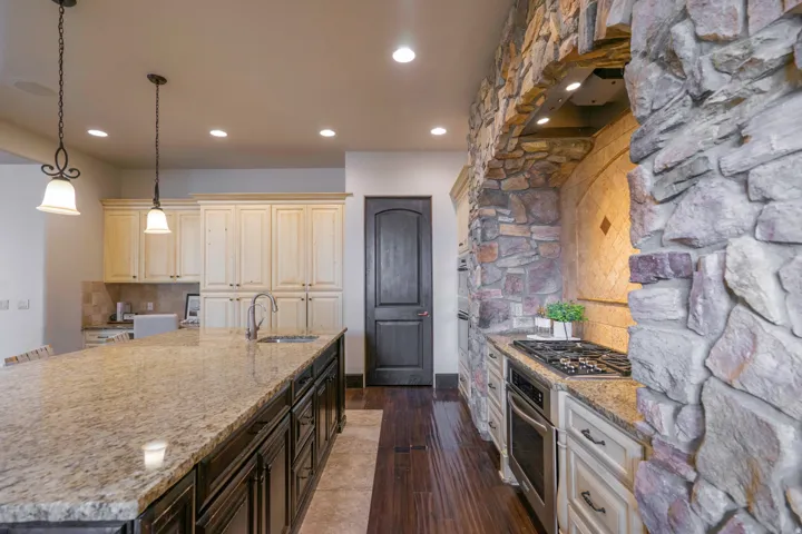 Gourmet kitchen featuring a stone-clad cooking alcove, built-in oven, gas cooktop, and an expansive island with a sink and pendant lighting