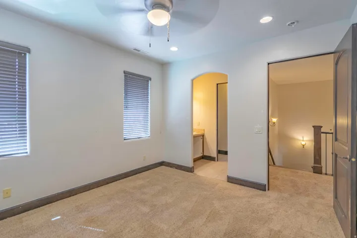 Carpeted flooring, two windows with blinds, ceiling fan, recessed lighting, and an arched entryway