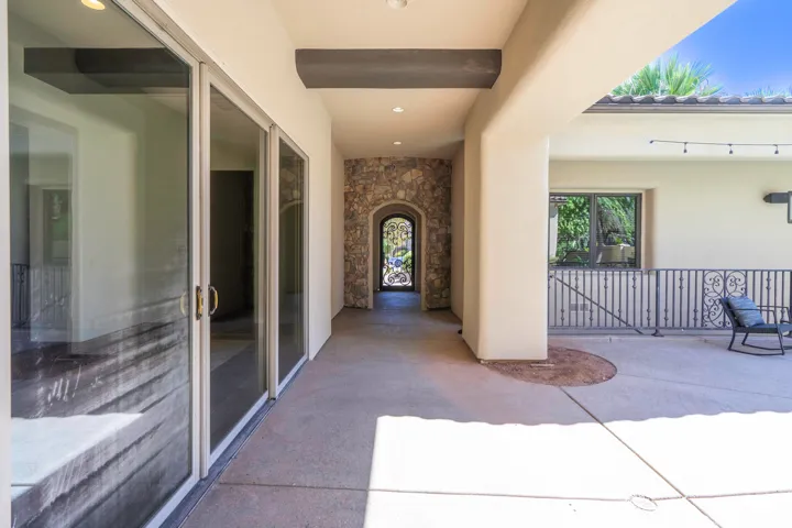 Covered outdoor patio with a concrete surface, stone archway, and iron railing