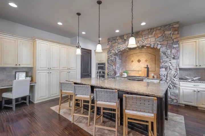 Spacious kitchen featuring a large central island with seating, stone-clad range hood, recessed lighting, and integrated desk area