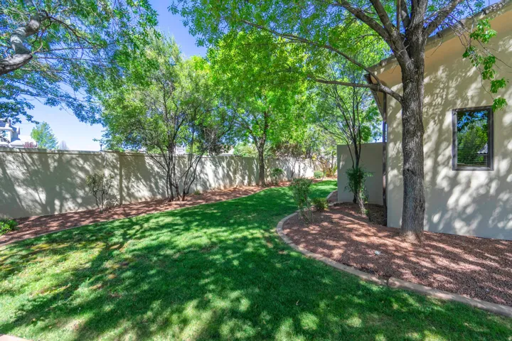 Expansive lawn area, mature trees, stucco exterior, and privacy wall
