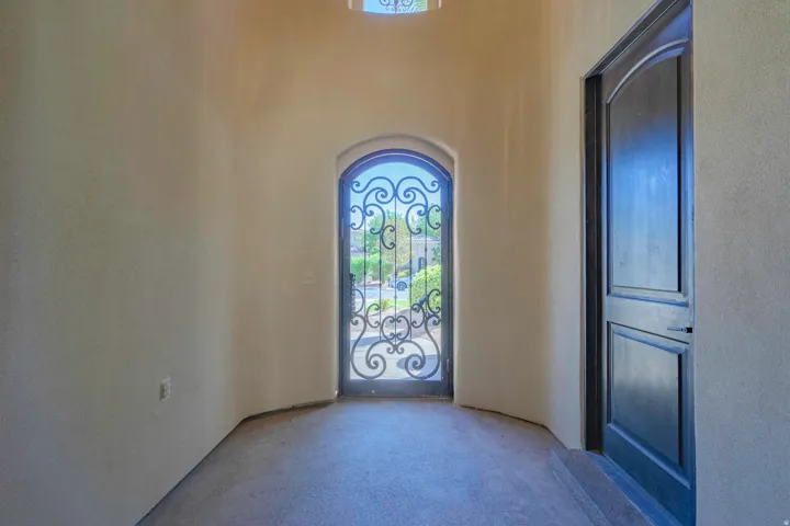 Arched entry with wrought iron door, wood-paneled interior door, and textured wall finishes