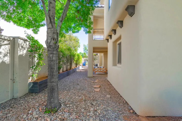 Side yard featuring a gravel ground cover, mature tree, stucco wall, and privacy landscaping