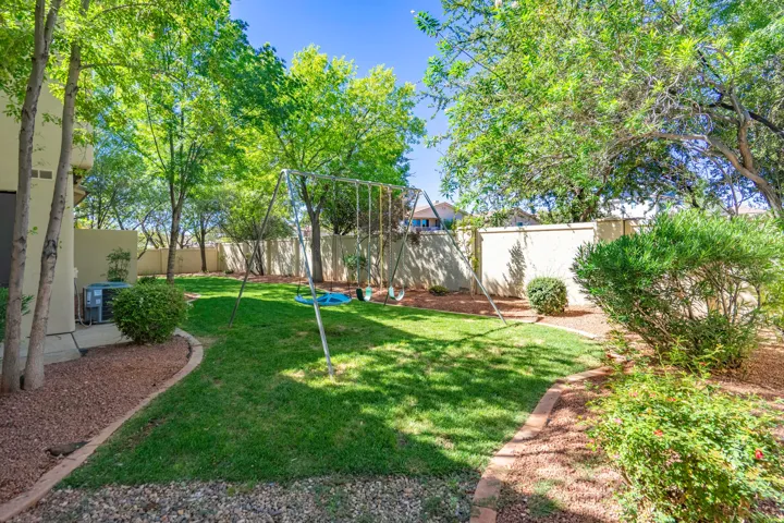 Expansive green lawn, mature trees providing shade, privacy wall, and defined landscaping beds