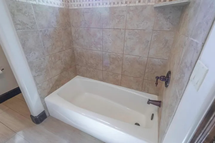 White built-in bathtub with tile surround, decorative mosaic accent tile, and bronze-finish fixtures
