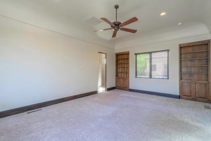 Carpeted room featuring a ceiling fan, recessed lighting, built-in shelving, and a window with blinds