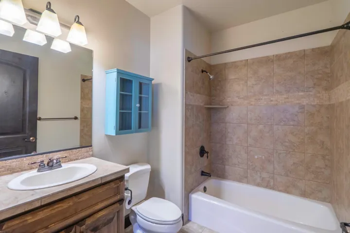 Bathroom featuring a wood-finish vanity with a single basin sink, tiled countertop, and a shower-tub combination with tiled walls