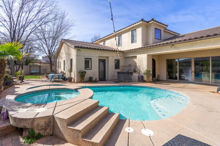 Expansive backyard featuring a custom pool and spa with integrated steps, a covered patio area, and a built-in outdoor kitchen
