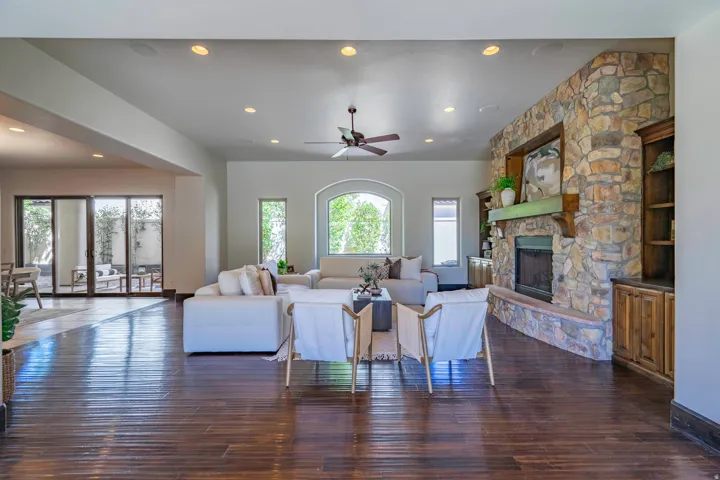 Spacious living area featuring dark wood-finish flooring, a stone-clad fireplace with a wood mantle, an arched window, and recessed lighting