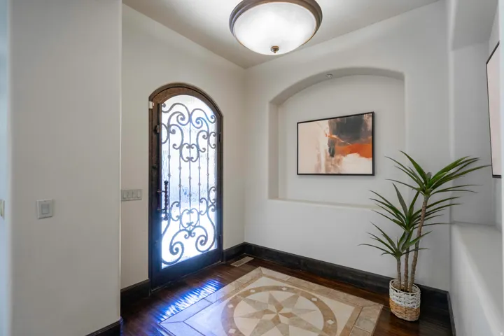 Arched wrought iron entry door, hardwood flooring, tile inlay, recessed wall niche, and flush mount ceiling light fixture