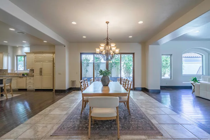 Recessed lighting illuminates a dining area with a multi-arm chandelier, wood-finish flooring, and tile flooring