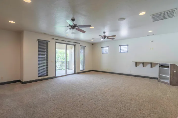 Spacious room featuring neutral carpeting, recessed lighting, two ceiling fans, and a built-in counter with cabinetry
